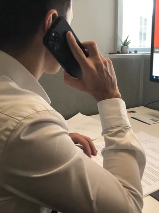 Рука с телефоном у уха на фоне рабочего стола с документами в офисе